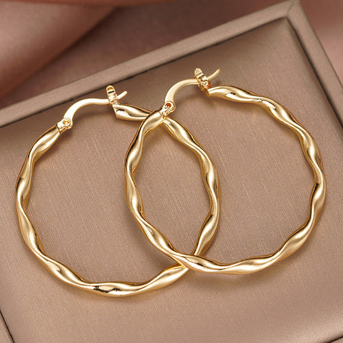 Gold wavy thin hoop earrings stacked on beige textured jewelry tray