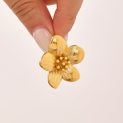 Hand holding single gold textured five-petal flower earring