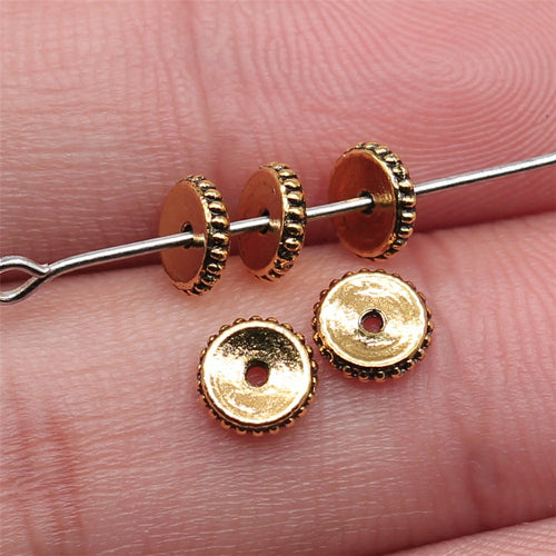 Antique Gold 齿边圆片小孔隔珠 displayed on fingertips