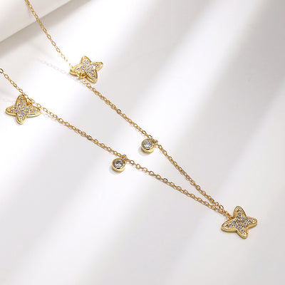 Gold tone star and butterfly station necklace with clear stones, product displayed in a styled close-up