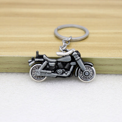 Silver-tone motorcycle keychain resting in front of a wooden ledge.