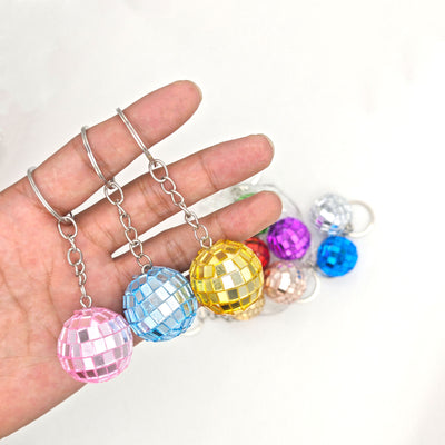 Hand holding pink blue and gold mirror disco ball keychains above color pile