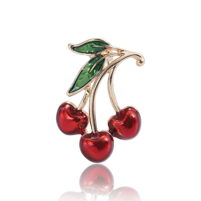 Front view of a gold-tone branch holding three glossy red cherries and green leaves