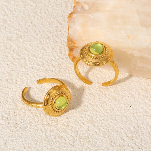 Two gold open disc rings with green glass on textured surface