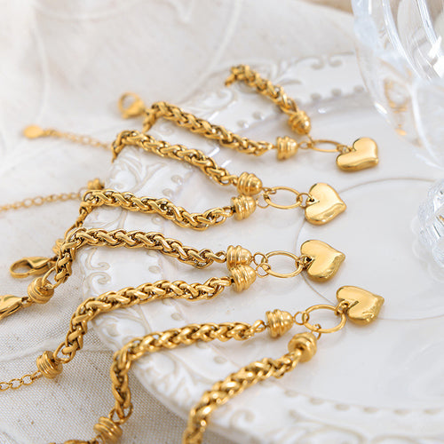 Multiple gold twisted rope heart charm bracelets on white ornate plate
