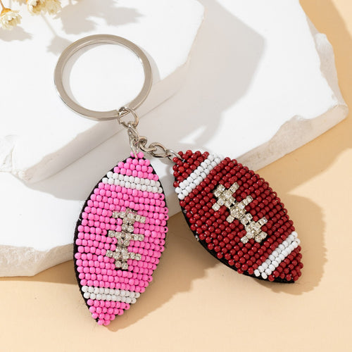 Two beaded football charms with rhinestone lace stitching hanging from a silver keyring