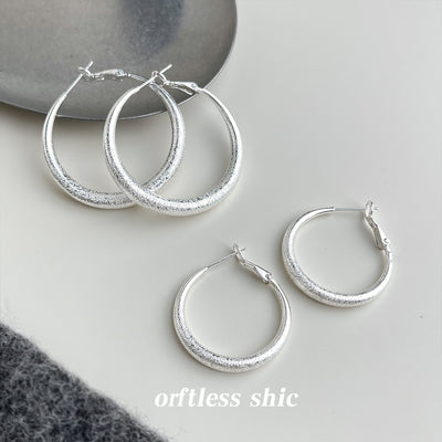 Two sizes of silver frosted thick tube hoops on white table