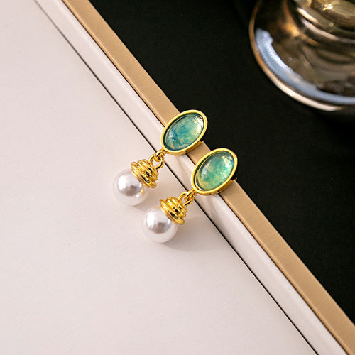 Teal green oval resin stud pearl drop earrings on white and black surface