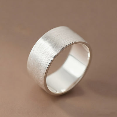 Silver brushed wide band ring angled close-up on beige