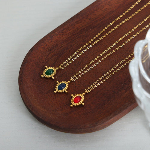 Three gold oval pendants green blue red on wooden tray