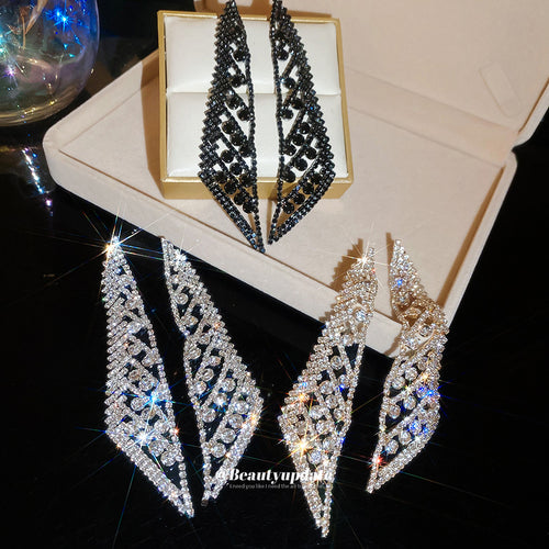 Close view of elongated crystal leaf earrings in gold, black, and silver tones