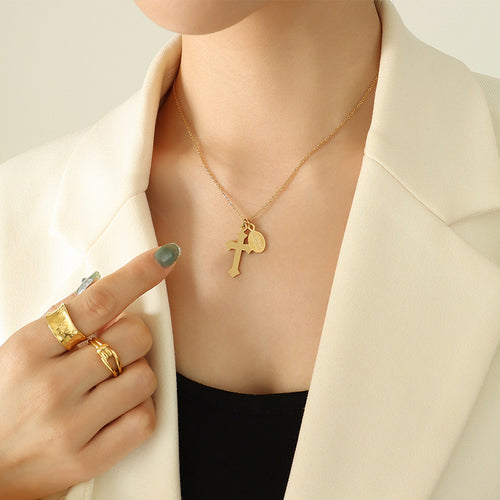 Gold cross and oval medal necklace worn on model collarbone