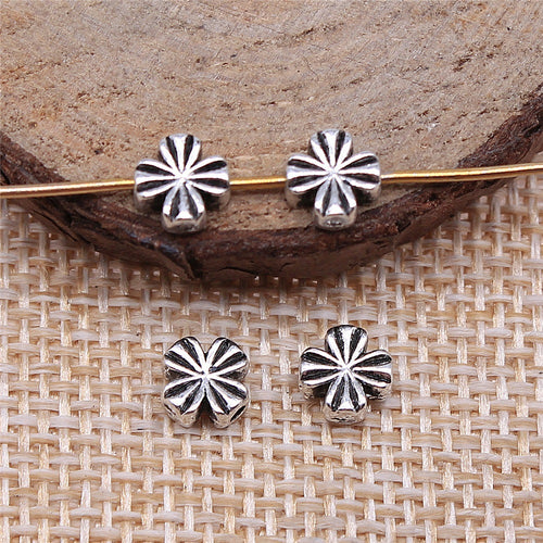 Single piece on a rustic surface of radiating flower small-hole metal bead in three finishes