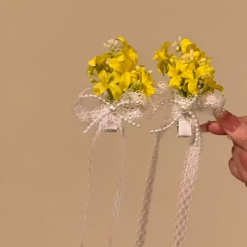Pair of yellow flower lace ribbon duckbill clips held against beige wall