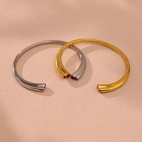 Gold and steel open cuff bracelets with heart ends on beige surface