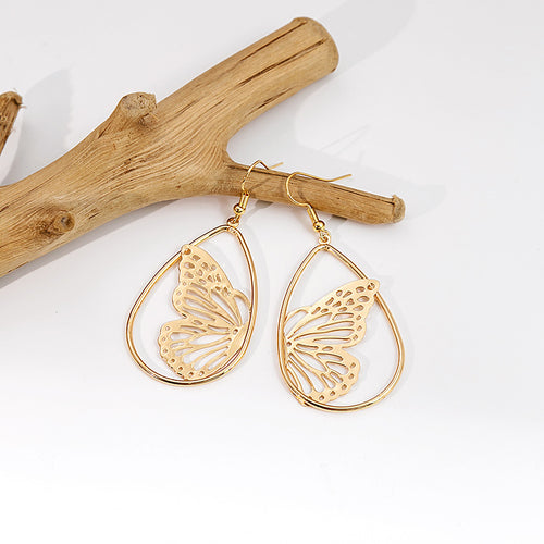 Gold butterfly teardrop dangle earrings hanging on driftwood branch