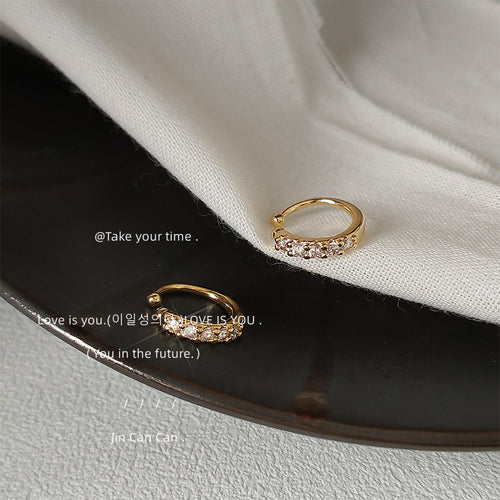 Gold-tone clear-stone fine-round huggie hoops shown worn on an ear.