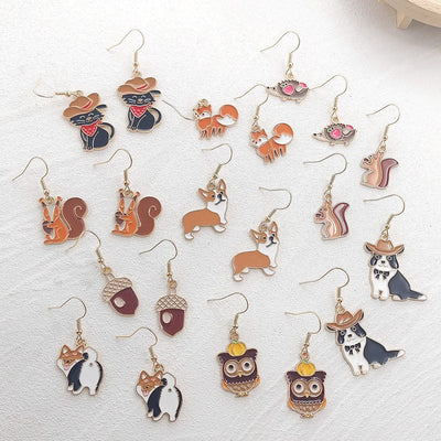 Assorted gold enamel animal and acorn drop earrings laid on white textured surface