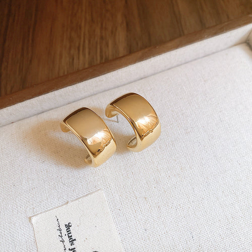 Five variations of smooth sculptural gold-tone teardrop hoops arranged for a close front view.
