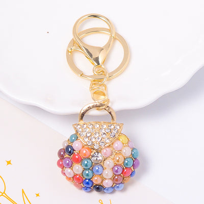 Multicolor pearl handbag keychain with gold handle on white dish