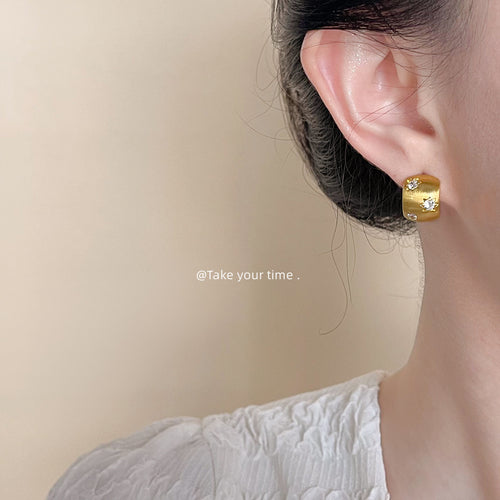 Brushed curved clear-stone studs shown worn in gold tone.