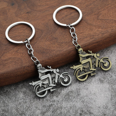 Two motorcycle rider keychains in silver and bronze tones on a wooden display.