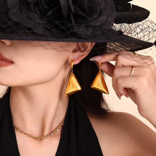 Model holding second gold triangle pyramid drop earring near face