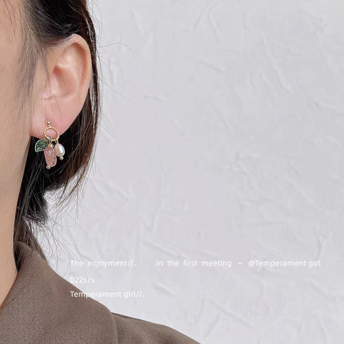 Gold-tone green-leaf pink-flower white-pearl studs shown worn on an ear.
