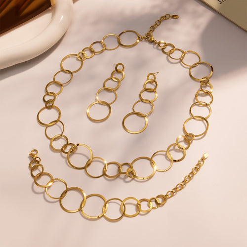 Flat lay gold circle link necklace bracelet and drop earrings on beige surface