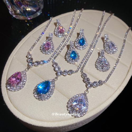 Three silver teardrop pendant sets in blue pink clear on oval tray
