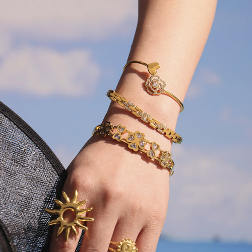 Wrist stack with gold clover heart bangle and other bracelets outdoors