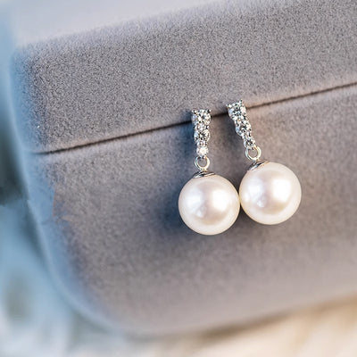 Pearl drop earrings with crystal bar posts on gray jewelry box