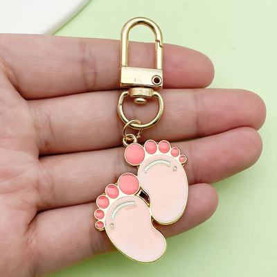 Pink baby feet keychain with a gold-tone swivel clasp held in a hand.