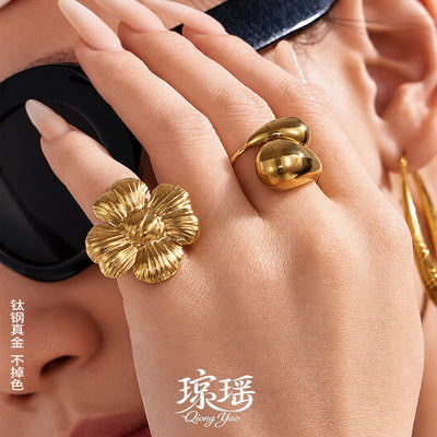 Styled hand view of sculptural flower and waterdrop open rings in main image 1.