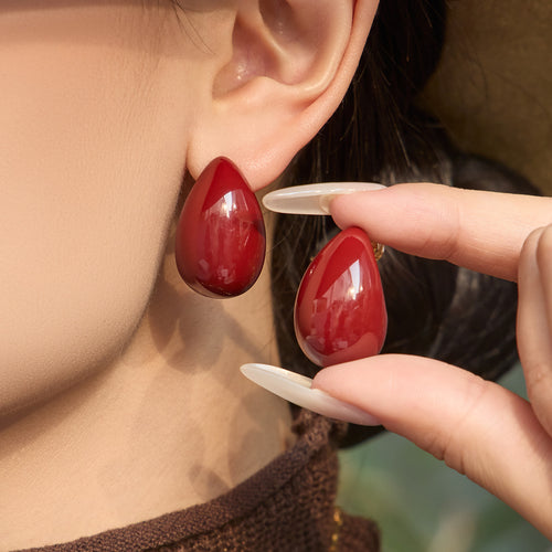 On-ear view of glossy burgundy teardrop stud earrings in main image 1.