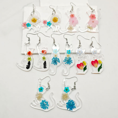 Assorted clear resin cat earrings with multicolor dried flowers laid on white board