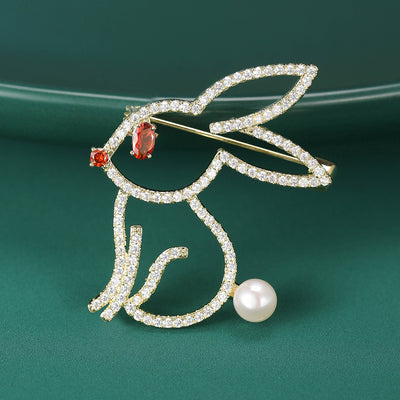 Gold outline rabbit brooch with pearl tail on green surface