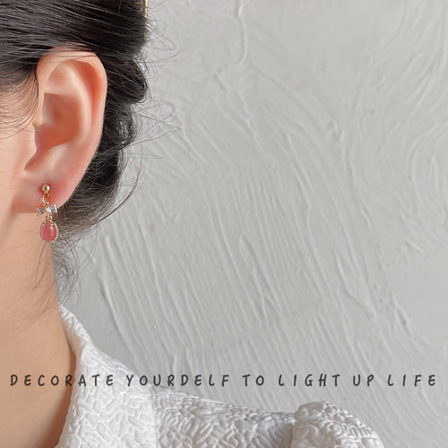 Pink cat eye bow drop earring worn on ear with white top