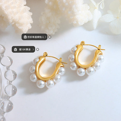 Pair gold U-hoops with pearl rims on white surface coral props