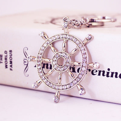 Close-up front view of a rhinestone ship wheel charm resting against a printed box.