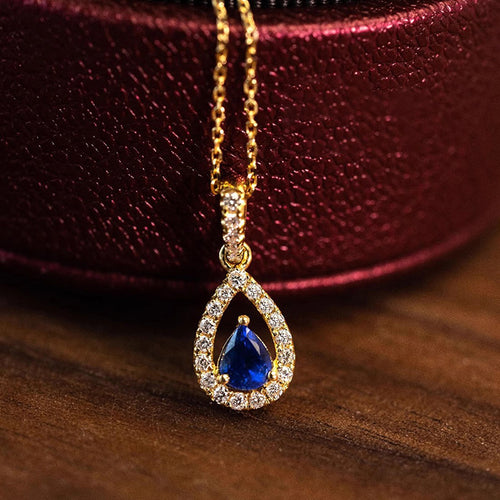 Gold blue pear pendant resting beside burgundy jewelry box on wood