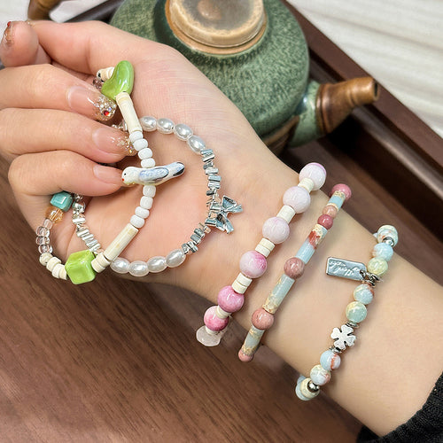 Hand wearing multiple mixed beaded bracelets with bird, bow, clover charms