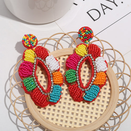 Multicolor beaded flower drop earrings with a rhinestone-lined center on a woven tray