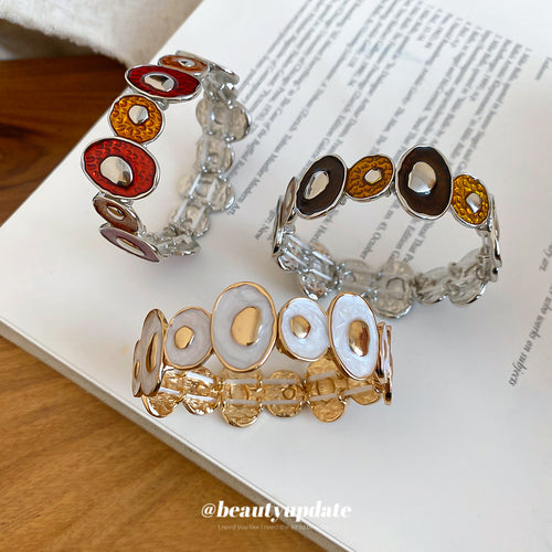 Three irregular enamel disc stretch bracelets in red brown and white colorways on book