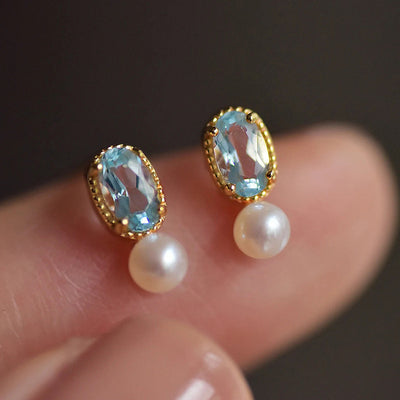 Gold blue stone pearl studs held close between fingers