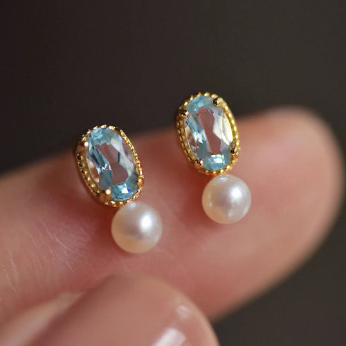 Gold blue stone pearl studs held close between fingers