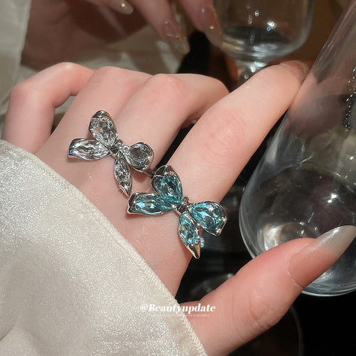 Clear and aqua-blue bow crystal rings worn stacked on finger