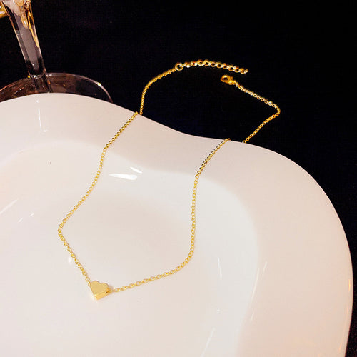 Gold heart pendant necklace on white dish with glass stem