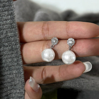 White faux pearl silver pavé disc drop stud earrings held on fingers