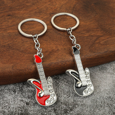 Two silver-tone guitar keychains with red and black accents displayed on wood and gray fabric.